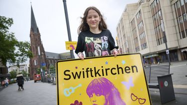 La estudiante Aleshanee Westhoff muestra un cartel de la ciudad Swiftkirchen en honor a Taylor Swift en Gelsenkirchen, Alemania, el martes 2 de julio de 2024. Los swifties están a punto de apoderarse de la ciudad alemana de Gelsenkirchen, donde la superestrella estadounidense Taylor Swift dará tres conciertos de su Eras Tour a finales de este mes. En honor al cantante, la ciudad se rebautizó como Swiftkirchen temporalmente para dar la bienvenida a las decenas de miles de fans. (Bernd Thissen/dpa via AP)