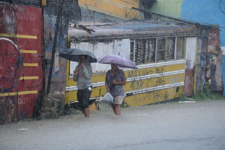 Dos personas caminan por una calle anegada a causa de las lluvias que dejó la tormenta tropical Melissa en Santo Domingo, República Dominicana, el 24 de octubre de 2025. (AP Foto/Ricardo Hernández)