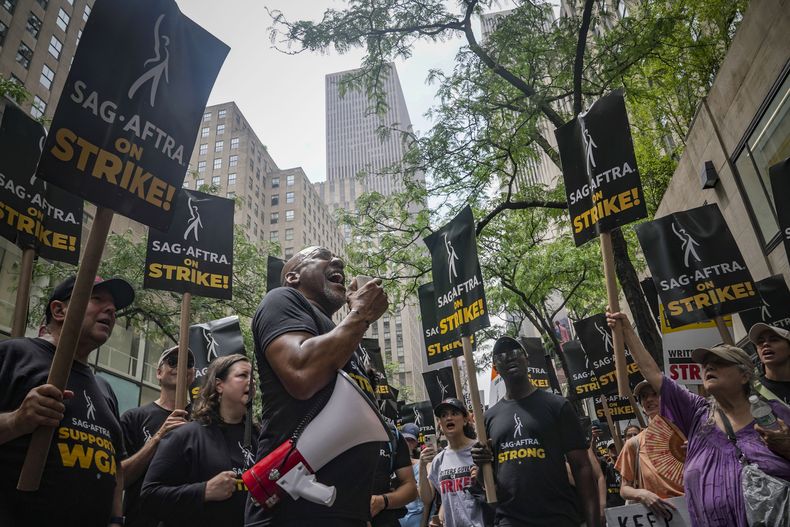 Ezra Knight, cuarto desde la izquierda, presidente local del sindicato de actores SAG-AFTRA en Nueva York usa un megáfono para dirigirse a guionistas y actores en huelga en un mitin el viernes 14 de julio de 2023, en NBC Universal Studios en Nueva York. (Foto AP/Bebeto Matthews)
