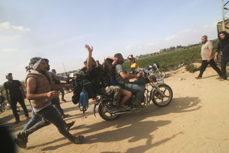 Palestinos llevan a una civil israelí capturada (centro), desde el kibutz de Kfar Azza a la Franja de Gaza, el 7 de octubre de 2023. Hamás, el grupo insurgente que gobierna la Franja de Gaza, llegó a cabo un ataque sin precedentes y por varios frente sobre Israel al amanecer del 7 de octubre, disparando miles de proyectiles mientras docenas de combatientes cruzaban la fortificada frontera para infiltrarse en varias localidades por tierra, mar y aire, tomando al país por sorpresa durante un importante feriado. (AP Foto)