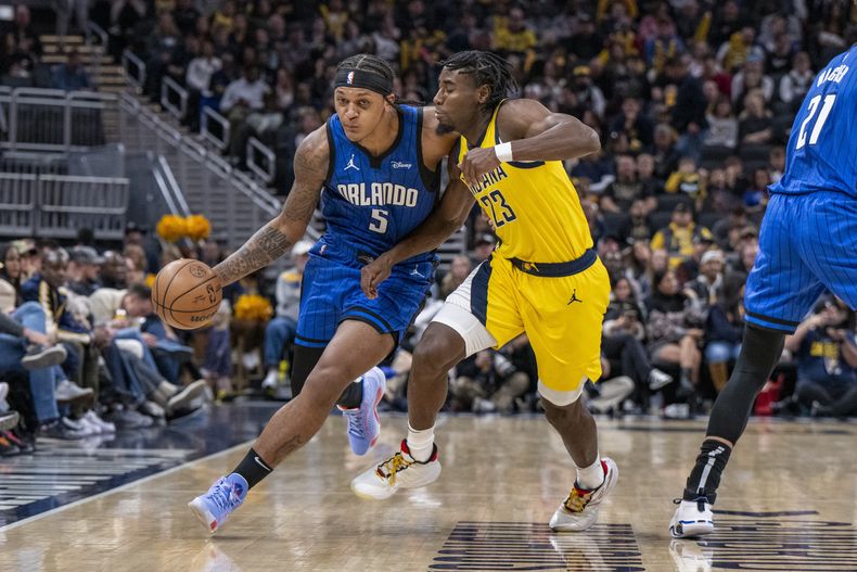 El alero del Magic de Orlando Paolo Banchero (5) conduce el balón ante el defensa de los Pacers de Indiana Aaron Nesmith (23) durante la primera mitad del juego de la NBA en Indianápolis, el domingo 19 de noviembre de 2023.(AP Foto/Doug McSchooler)