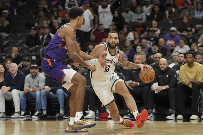 Tyrese Martin, de los Nets de Brooklyn, avanza frente a Oso Ighodaro, de los Suns de Phoenix, en el encuentro del miércoles 27 de noviembre de 2024 (AP Foto/Rick Scuteri)