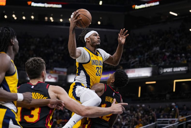 El pívot de los Pacers de Indiana, Myles Turner (33), dispara sobre el alero de los Hawks de Atlanta, DeAndre Hunter (12), durante la segunda mitad del partido de baloncesto de la NBA en Indianápolis, el domingo 14 de abril de 2024. (AP Foto/Michael Conroy)