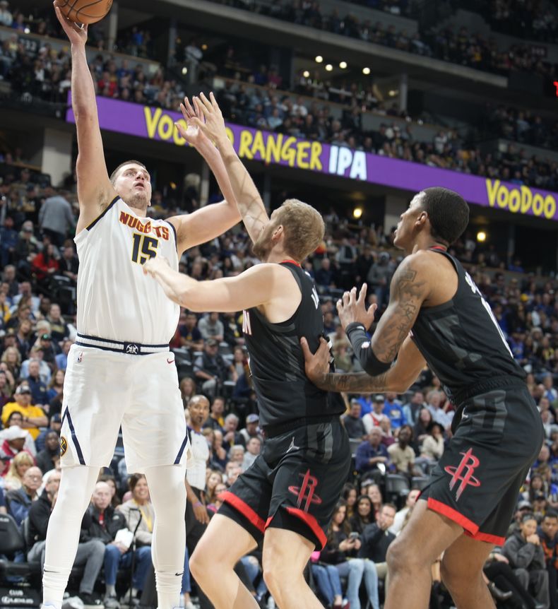 El pívot de los Nuggets de Denver Nikola Jokic salta para lanzar el balón a la canasta mientras lo defiende el pívot Jock Landale y el alero Jabari Smith Jr. de los Rockets de Houston en el encuentro del miércoles 29 de noviembre del 2023. (AP Foto/David Zalubowski)