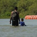 ARCHIVO - Dos migrantes caminan cerca de unas grandes boyas usadas como barrera fronteriza flotante en el Río Grande, o Bravo, el 1 de agosto de 2023, en Eagle Pass, Texas.. (AP Foto/Eric Gay, Archivo)
