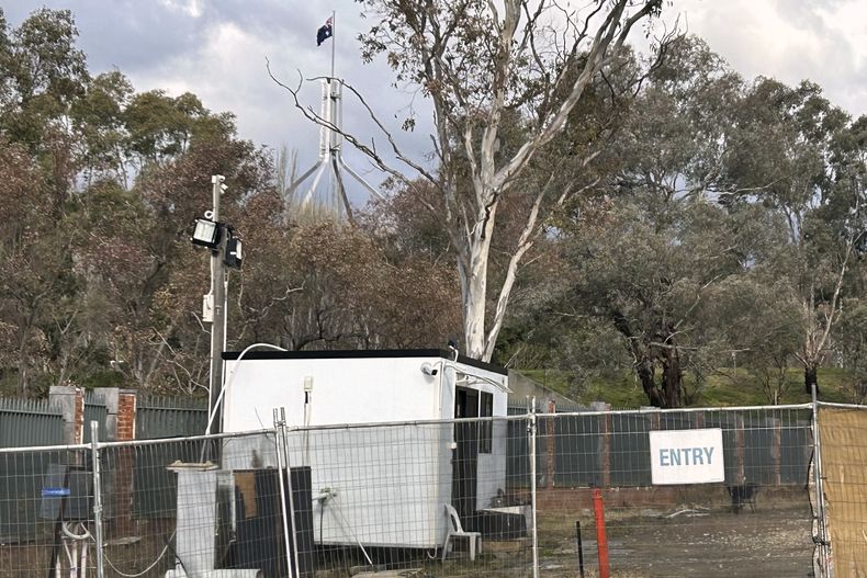 Una bandera del parlamento australiano ondea detrás de la cerca que rodea un edificio en los terrenos propuestos para una nueva embajada de Rusia en Canberra, el 23 de junio de 2023. (AP Foto/Rod McGuirk)