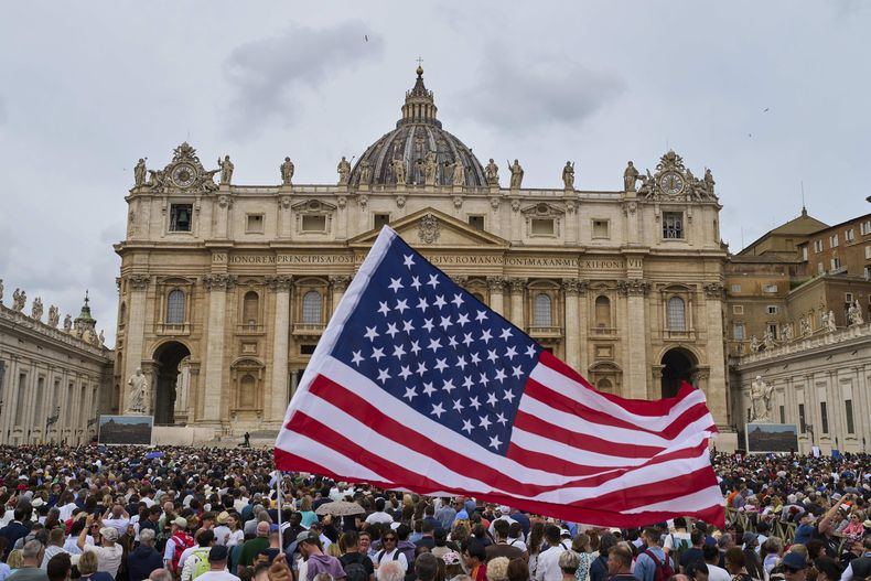 Una bandera de EEUU ondea en la multitud mientras el papa León XIV aparece en el balcón central de la Basílica de San Pedro para su primera bendición dominical después de su elección, el domingo 11 de mayo de 2025. (AP Foto/Bernat Armangue)