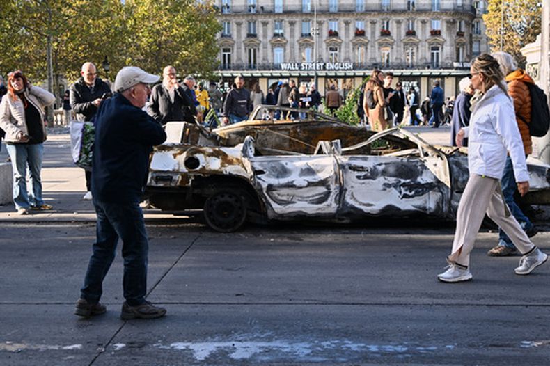 Gente mira a un auto calcinado en Place de la Republique el día después de una manifestación contra el creciente coste de la vida, que se suma a las protestas estudiantiles, en París, el domingo 18 de octubre de 2026. (AP Foto/Emma Da Silva)