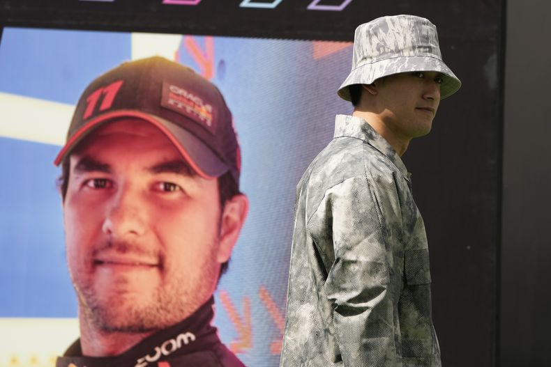 El piloto chino Zhou Guanyu, de Alfa Romeo, camina frente a una imagen del mexicano Sergio Pérez, de Red Bull, en la pista del Autódromo Hermanos Rodríguez en Ciudad de México, el jueves 26 de octubre de 2023 (AP Foto/Fernando Llano)