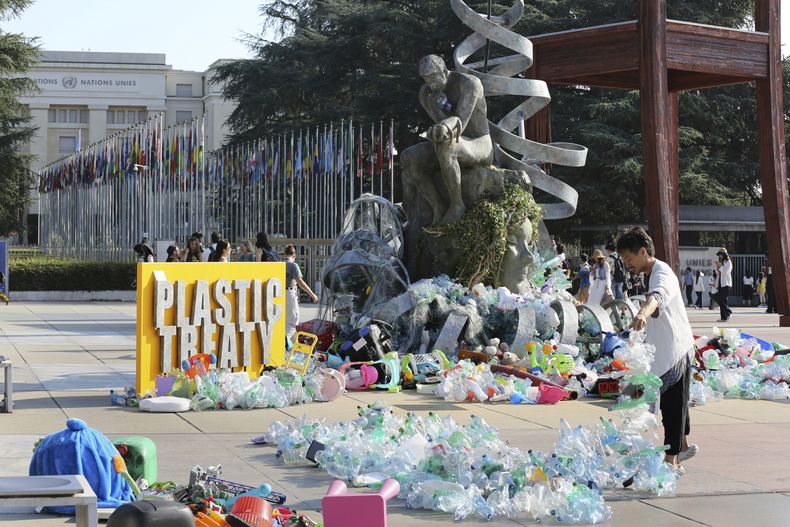 Benjamin Von Wong, a la derecha, un artista y activista canadiense, amontona pilas de desechos plásticos sobre una gran escultura que diseñó frente a la oficina de las Naciones Unidas en Ginebra, Suiza, el lunes 11 de agosto de 2025. (Foto AP/ Jennifer McDermott)