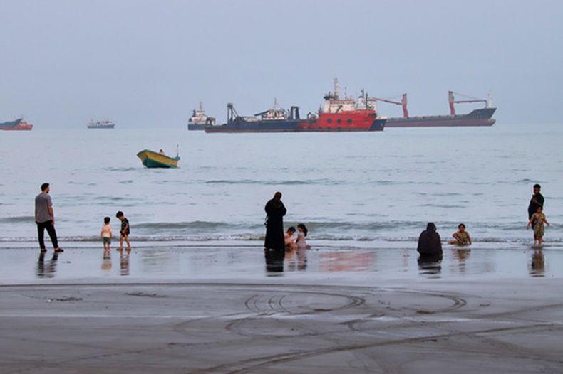 Gente pasando el tiempo en la playa mientras se ven embarcaciones comerciales fondeadas en el estrecho de Ormuz ante Bandar Abbas, Irán, el miércoles 5 de agosto de 2026. (Amirhosein Khorgooi/ISNA via AP)