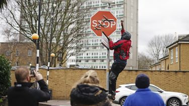 Una persona retira una obra de arte de Banksy que parece mostrar tres drones sobre un cartel de Stop que fue develado en la intersección de las calles Southampton Way y Commercial Way en Peckham, sureste de Londres, viernes 22 de diciembre de 2023. (Aaron Chown/PA via AP)