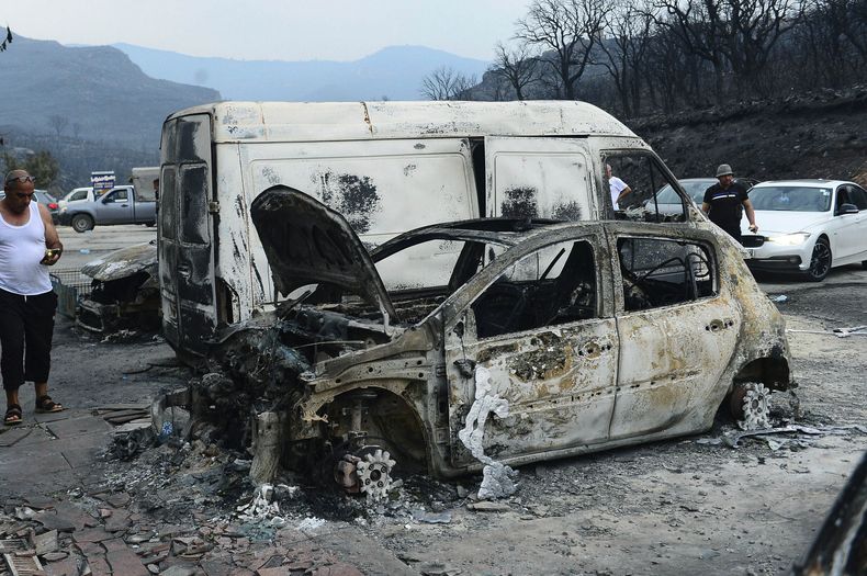 Gente inspecciona vehículos destruidos por las llamas en Bouira, a 100 kilómetros de Argel, 24 de julio de 2023. Al menos 25 personas han muerto a causa de los incendios, entre ellos varios soldados que ayudan a combatir las llamas en medio de fuertes vientos y temperaturas candentes. (AP Foto)