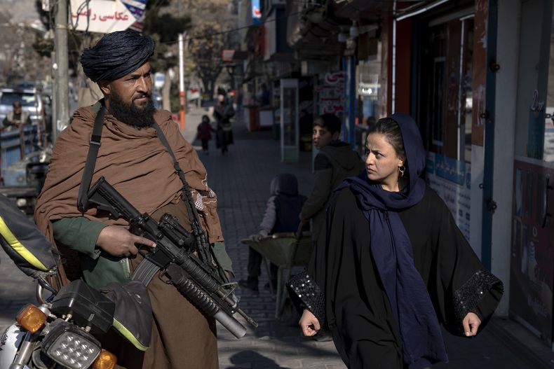 ARCHIVO - Un combatiente talibán monta guardia mientras una mujer pasa caminando en Kabul, Afganistán, el 26 de diciembre de 2022. Un reporte de Naciones Unidas publicado el 8 de mayo de 2023 condenaba al Talibán por su duro régimen desde que tomó el poder del país, con ejecuciones, amputaciones y fustigamientos públicos, así como por ignorar las peticiones internacionales de que respete las libertades y derechos humanos. (AP Foto/Ebrahim Noroozi, Archivo)