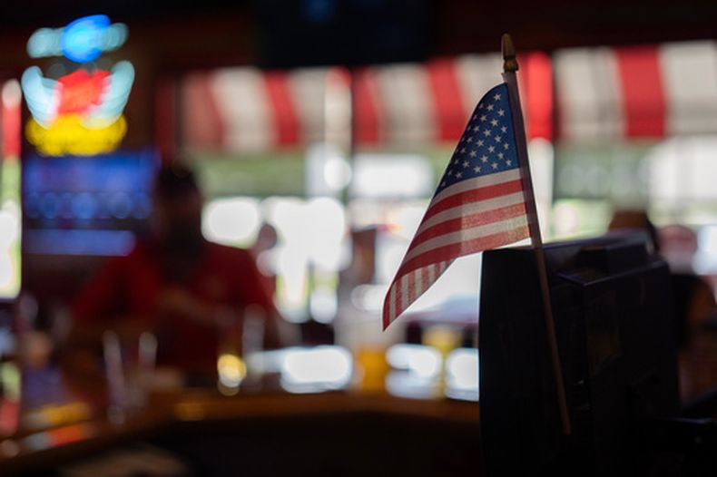 Una bandera estadounidense, en la caja registradora del bar Frickers en Springfield, Ohio, el 30 de septiembre de 2026, mientras los miembros del sindicato UAW Local 402 toman un trago en el último día de la antigua Navistar en su planta de Springfield. (AP Foto/Carolyn Kaster)