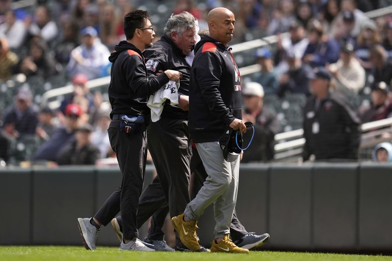 El umpire de primera base Hunter Wendelstedt, centro, camina fuera del campo asistido por personal médico después de recibir un golpe por un batazo de foul durante la séptima entrada del juego de béisbol de Grandes Ligas entre los Mellizos de Minnesota y los Mets de Nueva York, el miércoles 16 de abril de 2025, en Minneapolis. (AP Foto/Abbie Parr)