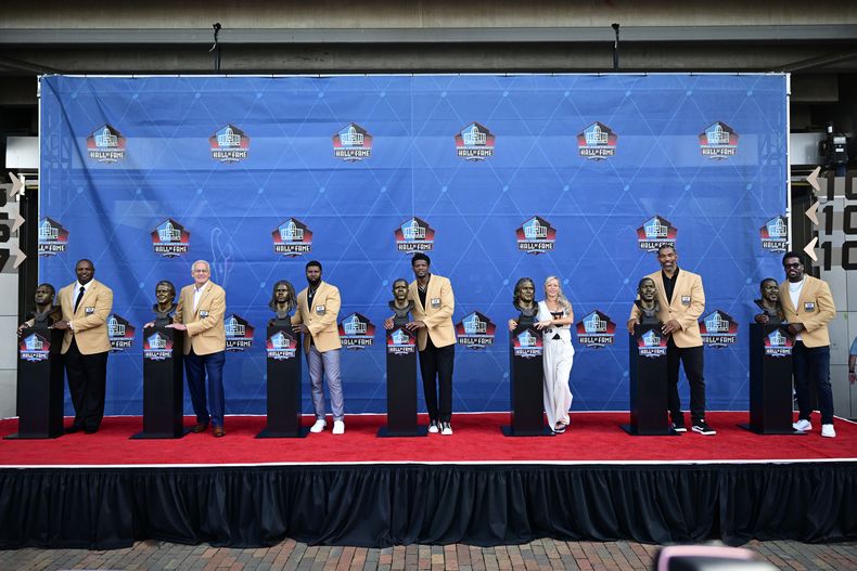 La clase 2024 del Salón de la Fama posa con sus busos durante la ceremonia de inducción en Canton, Ohio el sábado 3 de agosto del 2024. De izquierda a derecha: Dwight Freeney, Randy Gradishar, Devin Hester, Andre Johnson, Misty McMichael, wife of Steve McMichael, Julius Peppers, y Patrick Willis. (AP Foto/David Dermer)