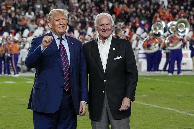 El expresidente y aspirante a la candidatura republicana Donald Trump hace un gesto junto al gobernador de Carolina del Sur, Henry McMaster, en el descanso de un partido del torneo universitario de fútbol americano NCAA entre la Universidad de Carolina del Sur y Clemson, el sábado 25 de noviembre de 2023, en Columbia, Carolina del Sur. (AP Foto/Chris Carlson)