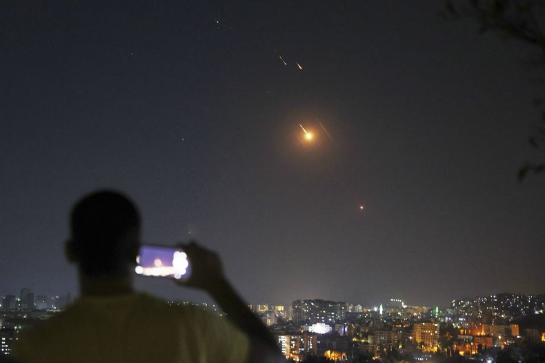 Un hombre toma una foto con su teléfono móvil mientras misiles lanzados desde Irán hacia Israel sobrevuelan Damasco, Siria, la madrugada del miércoles 18 de junio de 2025. (AP Foto/Ghaith Alsayed)