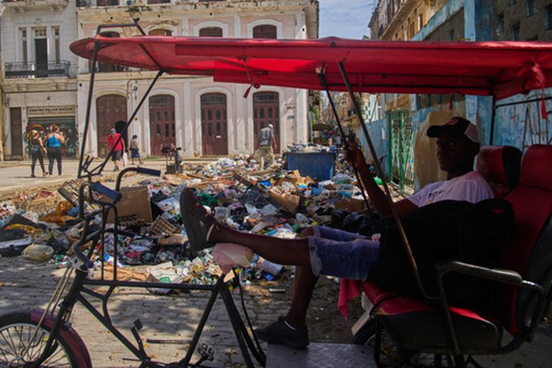 Un conductor de bicitaxi espera a los clientes junto a un montón de basura en La Habana, Cuba, el lunes 1 de junio de 2026. (Foto AP/Ramón Espinosa)