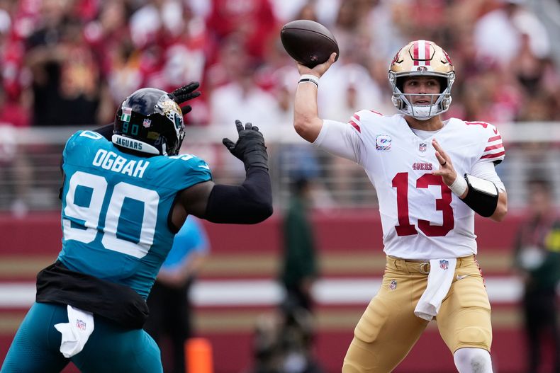 Brock Purdy (13), quarterback de los 49ers de San Francisco, lanza un pase mientras Emmanuel Ogbah (90), de los Jaguars de Jacksonville, lo presiona durante la primera mitad del partido de la NFL del domingo 28 de septiembre de 2025, en Santa Clara, California. (AP Foto/Godofredo A. Vásquez)