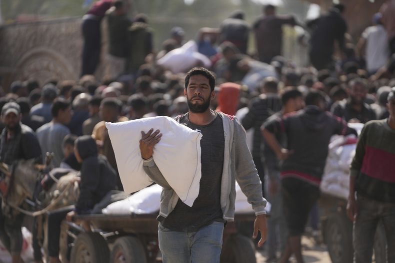 Palestinos se reúnen para recibir costales de harina distribuidos por la agencia de Naciones Unidas para los refugiados palestinos, UNRWA, el sábado 2 de noviembre de 2024, en Deir al Balah, Franja de Gaza. (AP Foto/Abdel Kareem Hana)