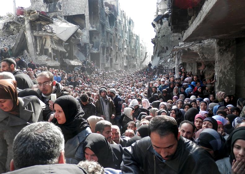 Esta foto tomada el 31 de enero de 2014 y proporcionada por la  Agencia de Naciones Unidas para los Refugiados Palestinos (UNRWA) se ven a habitantes de Yarmouk, una zona en Siria donde habitan palestinos, que acuden a recibir ayuda humanitaria. El confli