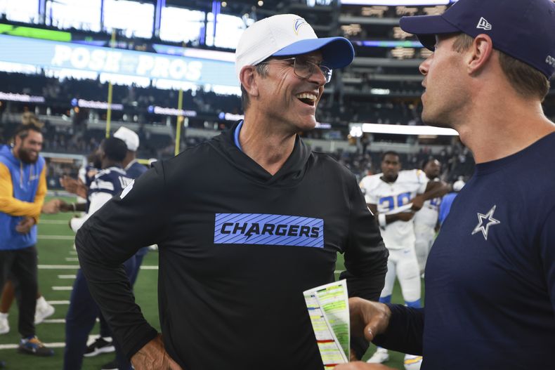 Jim Harbaugh, entrenador de los Chargers de Los Ángeles, habla con un integrante del cuerpo técnico de los Cowboys de Dallas, tras el partido de pretemporada disputado el sábado 24 de agosto de 2024 (AP Foto/Gareth Patterson)