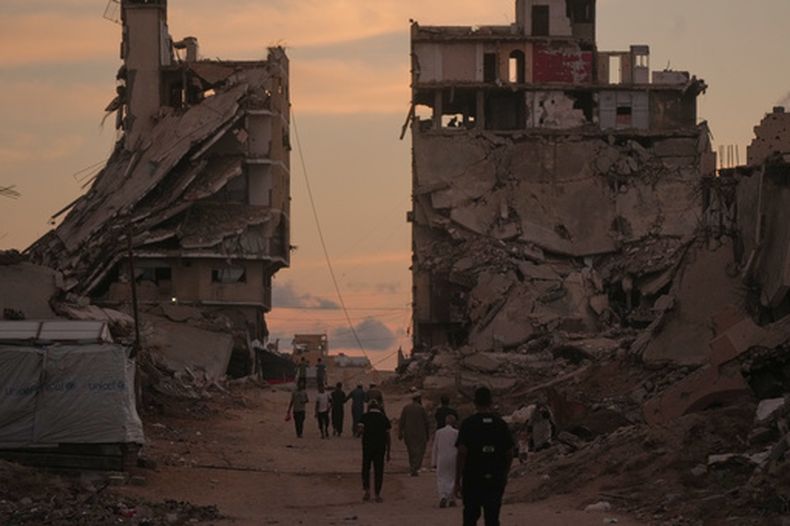 Varios palestinos caminan por una calle rodeada por edificios destruidos pr ataques militares israelíes durante la guerra entre Israel y Hamás en Ciudad de Gaza, el martes 6 de octubre de 2026. (AP Foto/Jehad Alshrafi)
