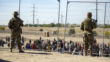 Migrantes esperan junto a una valla fronteriza mientras son vigilados por miembros de la Guardia Nacional de Texas, para ingresar a El Paso, Texas, el miércoles 10 de mayo de 2023. (AP Foto/Andres Leighton)
