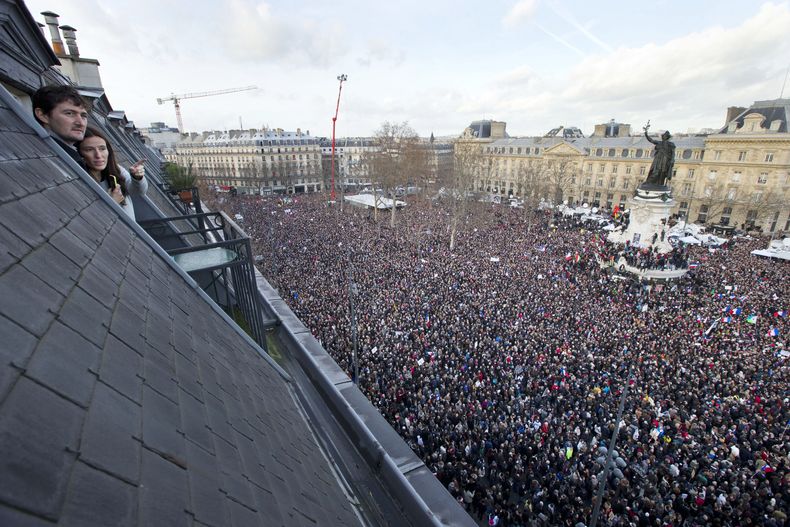 ARCHIVO - Dos personas observan desde su apartamento mientras miles de personas se reúnen en la Plaza de la República en París, Francia, el domingo 11 de enero de 2015, luego de una masacre en el periódico satírico Charlie Hebdo. (AP Foto/Peter Dejong, archivo)