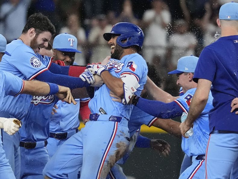 Marcus Semien (centro), de los Rangers de Texas, es felicitado por sus compañeros luego de conectar un sencillo que remolcó al dominicano Leody Taveras en el 9no episodio del juego de béisbol ante los Marineros de Seattle, el domingo 22 de septiembre de 2024, en Arlington, Texas. (AP Foto/LM Otero)