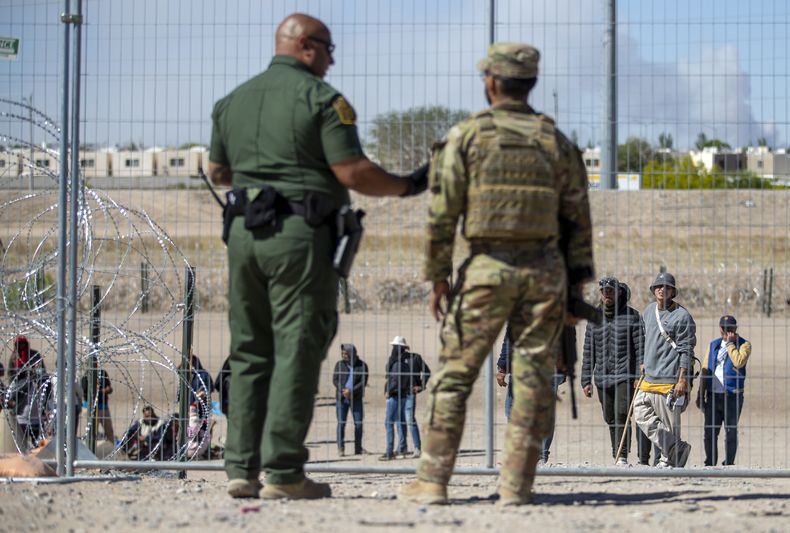 Migrantes aguardan a un costado del muro fronterizo vigilado por la Patrulla Fronteriza y la Guardia Nacional de Texas el miércoles 10 de mayo de 2023, con el fin de ingresar a El Paso, Texas. A partir del jueves, el gobierno del presidente Joe Biden comenzará a negarle el asilo a los migrantes que se presenten en la frontera con México sin primero haber presentado una solicitud en línea o pedido protección en el país por el que pasaron, según una nueva medida dada a conocer el miércoles. Las autoridades federales han advertido de complicaciones en los próximos días en un momento en que expira la medida conocida como Título 42, la cual permitía expulsar rápidamente a migrantes para prevenir la propagación del COVID-19. (AP Foto/Andrés Leighton)