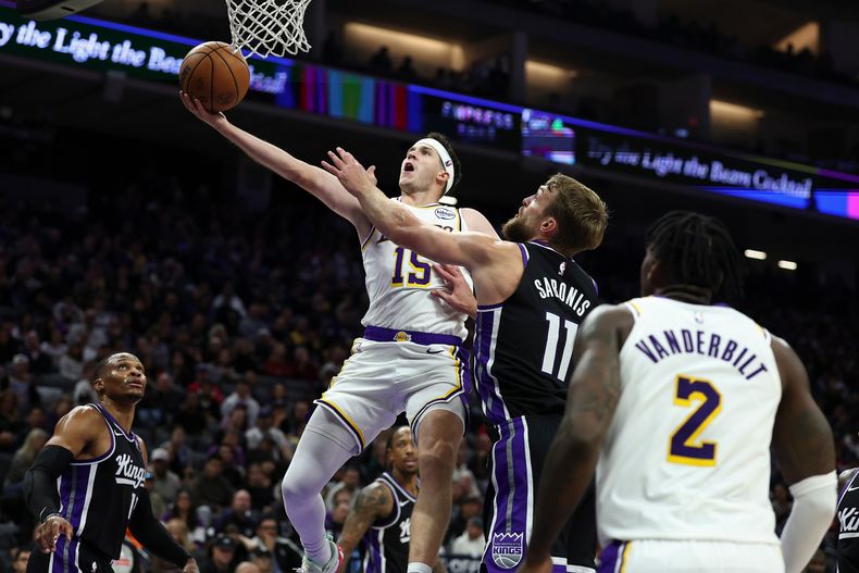 Austin Reaves, izquierda, de los Lakers de Los Ángeles, recibe una falta de Domantas Sabonis (11), de los Kings de Sacramento, durante la primera mitad del juego de baloncesto de la NBA, el domingo 26 de octubre de 2025, en Sacramento, California. (AP Foto/Sara Nevis)