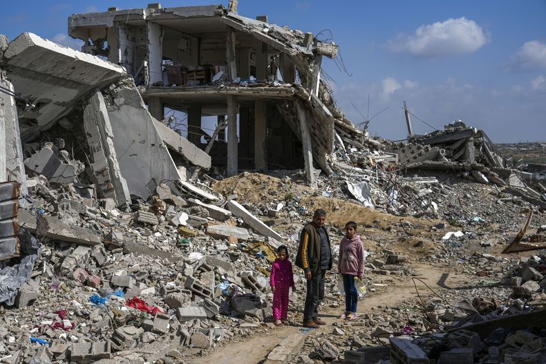 Un hombre palestino y dos niñas observan los escombros de viviendas destruidas por la ofensiva aérea y terrestre del ejército de Israel contra Hamás en el campamento para refugiados Bureij, en el centro de la Franja de Gaza, el lunes 27 de febrero de 2025. (AP Foto/Abdel Kareem Hana)