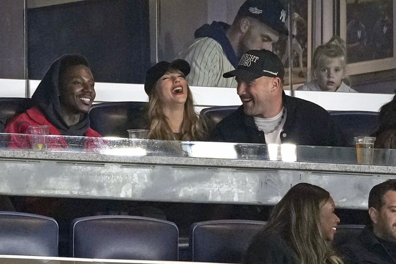 ARCHIVO - Travis Kelce, a la derecha, y Taylor Swift con el actor y comediante Jerrod Carmichael, a la izquierda, en el Juego 1 de la Serie de Campeonato de la Liga Americana de béisbol entre los Guardianes de Cleveland y los Yanquis de Nueva York, el 14 de octubre de 2024, en Nueva York. (Foto AP/Seth Wenig, archivo)
