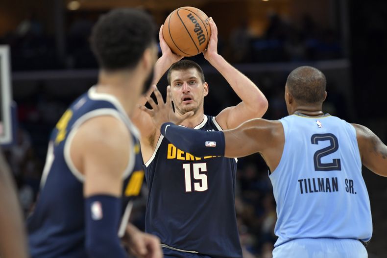 El pívot de los Nuggets de Denver Nikola Jokic (15) mira a quien pasar el balón mientras es defendido por el alero de los Grizzlies de Memphis Xavier Tillman Sr. (2) durante la 2da mitad del juego de NBA, en Memphis, Tennessee, el viernes 27 de octubre de 2023. (AP Foto/Brandon Dill)