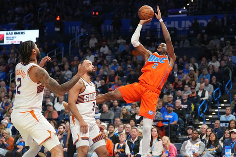 Shai Gilgeous-Alexander (2), del Thunder de Oklahoma City, dispara sobre Nick Richards (2) y Dillon Brooks (3), de los Suns de Phoenix durante la segunda mitad del juego de baloncesto de la Copa NBA, el miércoles 10 de diciembre de 2025, en Oklahoma City. (AP Foto/Kyle Phillips)
