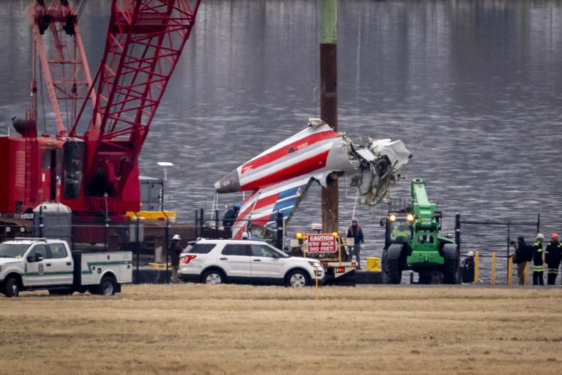 Una grúa descarga una pieza de los restos de un buque de salvamento en un camión de plataforma, cerca del lugar de los restos en el río Potomac de una colisión en pleno vuelo entre un avión de American Airlines y un helicóptero Black Hawk, en el Aeropuerto Nacional Ronald Reagan de Washington, el miércoles 5 de febrero de 2025, en Arlington, Virginia. (AP foto/Ben Curtis)