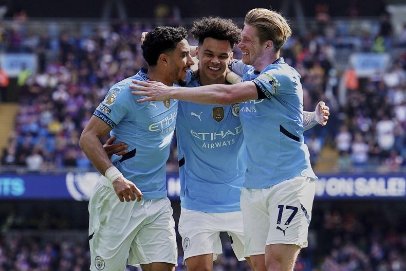 Nico OReilly del Manchester City celebra con sus compañeros Omar Marmoush y Kevin De Bruyne tras anotar en el encuentro de la Liga Premier ante el Crystal Palace el sábado 12 de abril del 2025. (Martin Rickett/PA via AP)