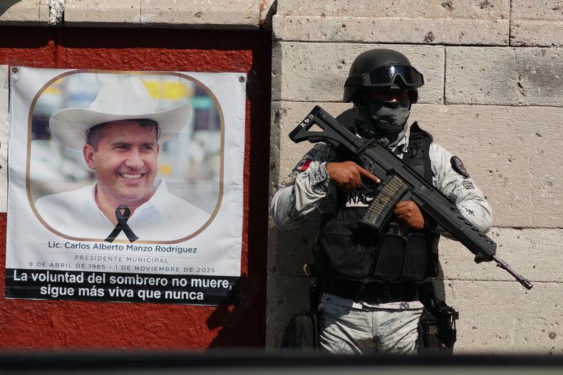 Un soldado de la Guardia Nacional, junto a una imagen del difunto alcalde Carlos Manzo Rodríguez en Uruapan, México, mientras fiscales del estado de Michoacán arrestan a sospechosos en la investigación de su asesinato, el 21 de noviembre de 2025. (AP Foto/Eduardo Verdugo)