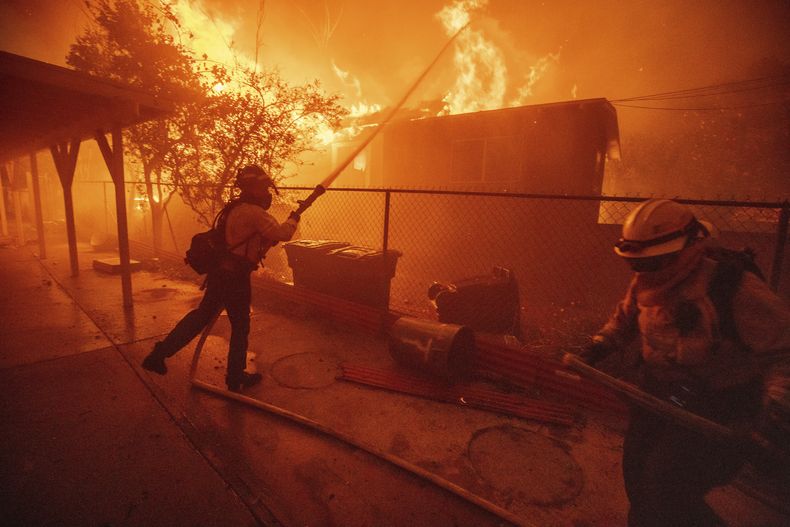 ARCHIVO - Dos bomberos intentan proteger una estructura mientras el incendio Eaton avanza el 8 de enero de 2025, en Altadena, California. (AP Foto/Ethan Swope, archivo)