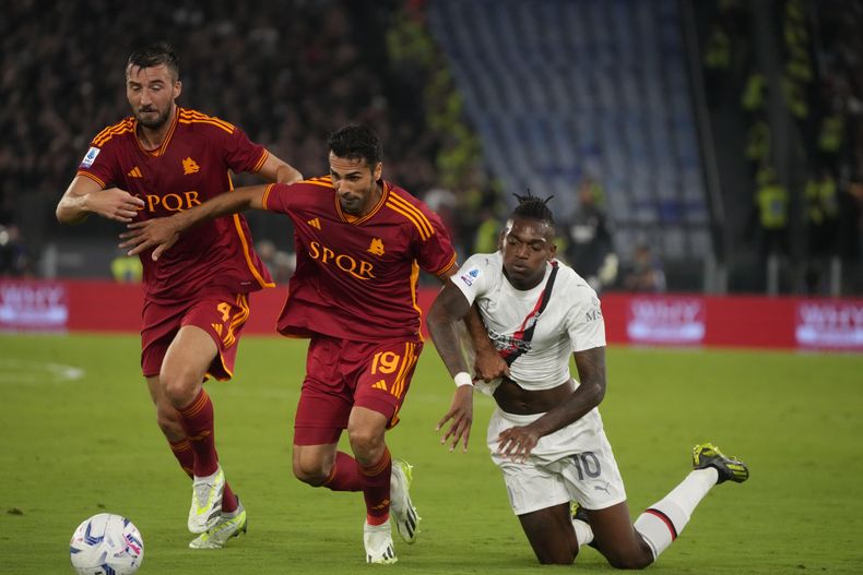 Rafael Leão del AC Milán cae mientras disputa la pelota ante los jugadores de la Roma Bryan Cristante (izquierda) y Zeki Celik (centro) durante el partido jugado en el Estadio Olímpico de Roma en la Liga Italiana. Viernes 1 de septiembre de 2023. (AP Foto/Gregorio Borgia)