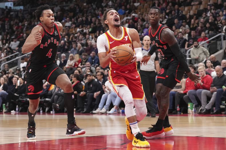 Trae Young, base de los Hawks de Atlanta, intenta encestar delante de Scottie Barnes (4) y del base Dennis Schroder (17), de los Raptors de Toronto, en el encuentro del viernes 15 de diciembre de 2023 (Chris Young/The Canadian Press via AP)