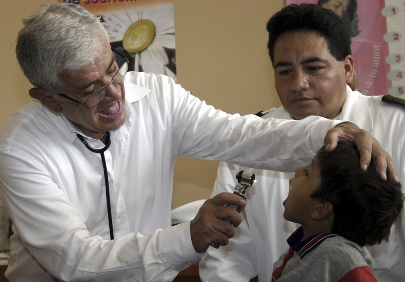 ARCHIVO - El presidente de Ecuador, Alfredo Palacio, examina a un niño durante la inauguración del Centro Nacional de Atención en Frontera, un centro ubicado en San Miguel, en la frontera con Colombia, el 14 de diciembre de 2006. (AP Foto/Cecilia Puebla, Archivo)