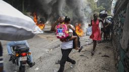 Varias personas corren junto a neumáticos en llamas durante una protesta contra el primer ministro Ariel Henry, el lunes 5 de febrero de 2024, en Puerto Príncipe, Haití. (AP Foto/Odelyn Joseph)