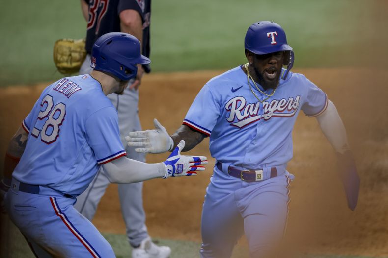 El cubano Adolis García (derecha) celebra junto a Jonah Heim (izquierda) luego de anotar la carrera de la ventaja en la octava entrada del juego ante los Guardianes de Cleveland, en Arlington, Texas. Domingo 16 de julio de 2023. (AP Foto/Gareth Patterson)