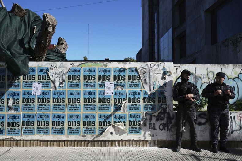 Carteles con la frase Justice para Dios cubren un muro donde dos policías esperan afuera del tribunal donde se realiza el juicio por la muerte de Diego Maradona, por supuestos desmanejos en el cuidado de la salud del astro. (AP Foto/Rodrigo Abd)