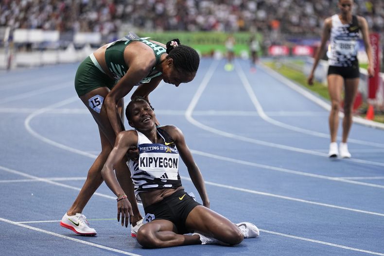 La keniana Faith Kipyegon recibe ayuda para ponerse de pie por parte de la también keniana Beatrice Chepkoech (izquierda) tras ganar los 5.000 metros y batir el récord mundial en la justa de París de la Liga Diamante, el viernes 9 de junio de 2023. (AP Foto/Michel Euler)