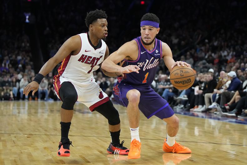 El armador de los Suns de Phoenix Devin Booker (derecha) conduce ante el base del Heat de Miami Kyle Lowry (izquierda), durante la primera mitad del juego de baloncesto de la NBA, el viernes 5 de enero de 2024, en Phoenix. (AP Foto/Rick Scuteri)